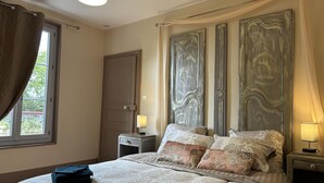 A bedroom with a large bed, two nightstands, a window with curtains, and a door. - Historic 1830 Mansion with Spa, Games, Pets Allowed (Jaligny-sur-Besbre)