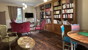 A library with wooden bookshelves, a television, and classic furniture. - Historic 1830 Mansion with Spa, Games, Pets Allowed (Jaligny-sur-Besbre)