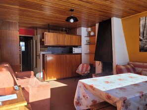 A compact room with wooden cabinets, a kitchenette, a bed with a floral bedspread, and a small table.