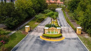 Una entrada vigilada con una fuente, rodeada de vegetación exuberante y un camino pavimentado.
