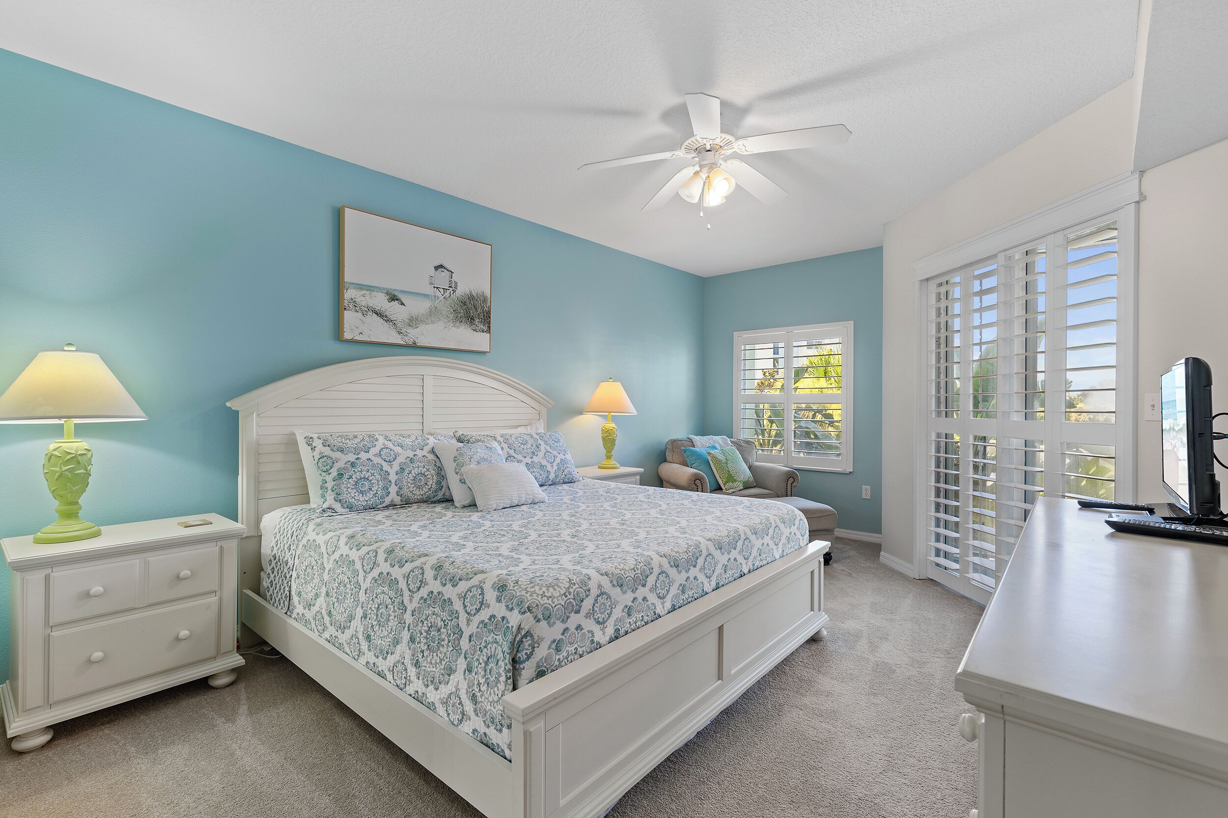 A bedroom with a bed, nightstands, a desk, a ceiling fan, and a window with blinds.