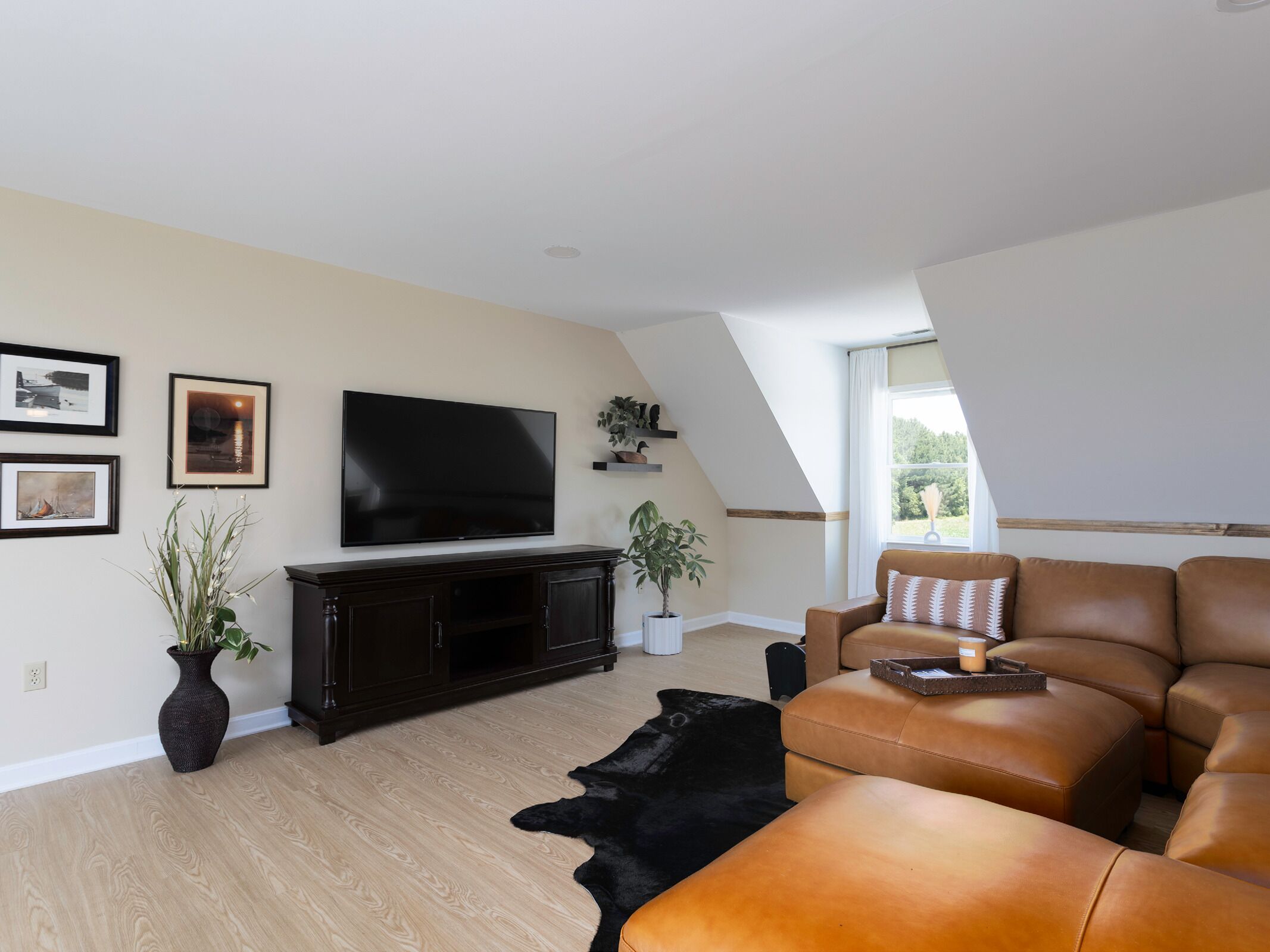 Een moderne woonkamer met een flatscreen televisie, een entertainmentmeubel van donker hout, een leren bank en een zwart vloerkleed.