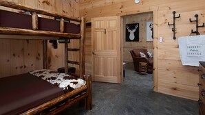 Una habitación de madera con literas, una puerta que da a otra habitación, un sofá y una bolsa de ropa para el servicio de lavandería.
