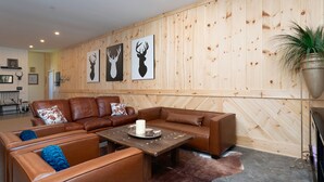 Una sala de estar moderna con sofás de cuero, una pared de madera con un arte de cabeza de venado montado, una mesa de centro y una planta en maceta.