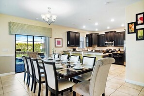 A modern kitchen with dark cabinetry, a dining area with a glass table, and a view of a pool.