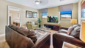 A living room with a brown leather sofa, a green armchair, and a coffee table. There is a flat-screen TV mounted on the wall, a ceiling fan, and a window with blinds. - Close to Disney! Private Pool-Spa! Game Room! (Kissimmee)