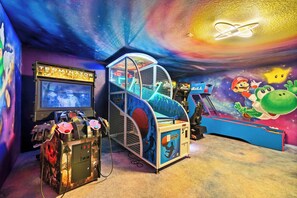 A gaming arcade with various machines, including a basketball game and a racing game. - Resort Access 6BR Pool Home w Arcade near Disney (Kissimmee)