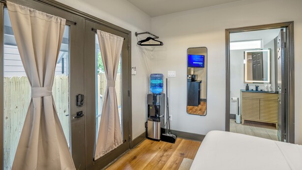 A hotel room with a bed, a water dispenser, a mirror, and a view of the outside. - HTX Ultra Hotel Suite #2 (Houston)