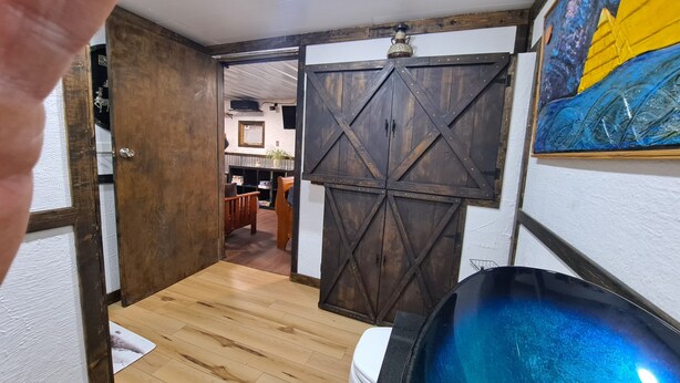 Una habitación con piso de madera, una tina azul grande y una puerta de estilo rústico tipo granero.