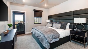 Une chambre moderne avec un grand lit, un ventilateur de plafond, une table de chevet avec une lampe et une vue sur l’extérieur par une porte.