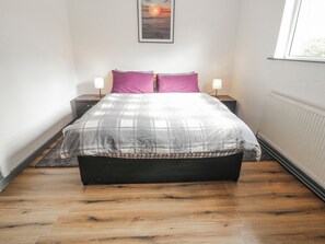 A bedroom with a bed, two bedside tables, a nightstand, a radiator, and a framed picture on the wall. - THE ISLAND'S VIEW, pet friendly in Gortahork, County Donegal (LETTERKENNY)