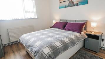 Un dormitorio con cama, mesita de noche, lámpara y un cuadro en la pared.