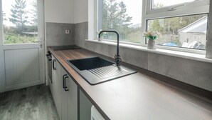 A modern kitchen with a built-in sink, wooden countertop, and a window with a view of greenery. - THE ISLAND'S VIEW, pet friendly in Gortahork, County Donegal (LETTERKENNY)