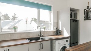 A modern kitchen with a built-in washing machine, a sink, and a window with a view of the outside. - THE ISLAND'S VIEW, pet friendly in Gortahork, County Donegal (LETTERKENNY)