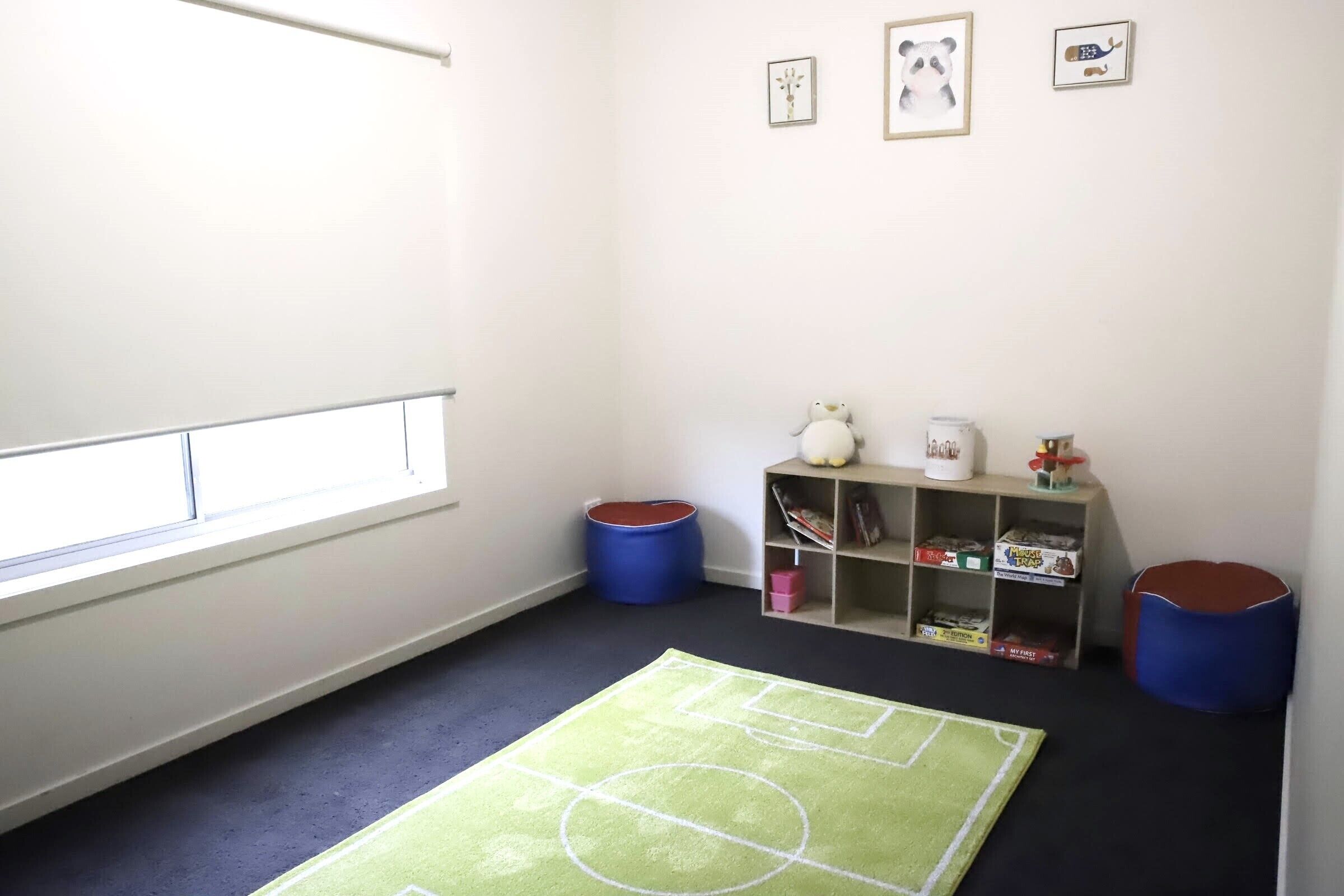 A room with a window, a green rug with white lines, a bookshelf, and two blue bean bags.