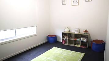 A room with a window, a green rug with white lines, a bookshelf, and two blue bean bags.