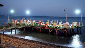 Un muelle con hileras de sillas y sombrillas de playa, un flotador salvavidas y un cartel que indica prohibido bañarse.