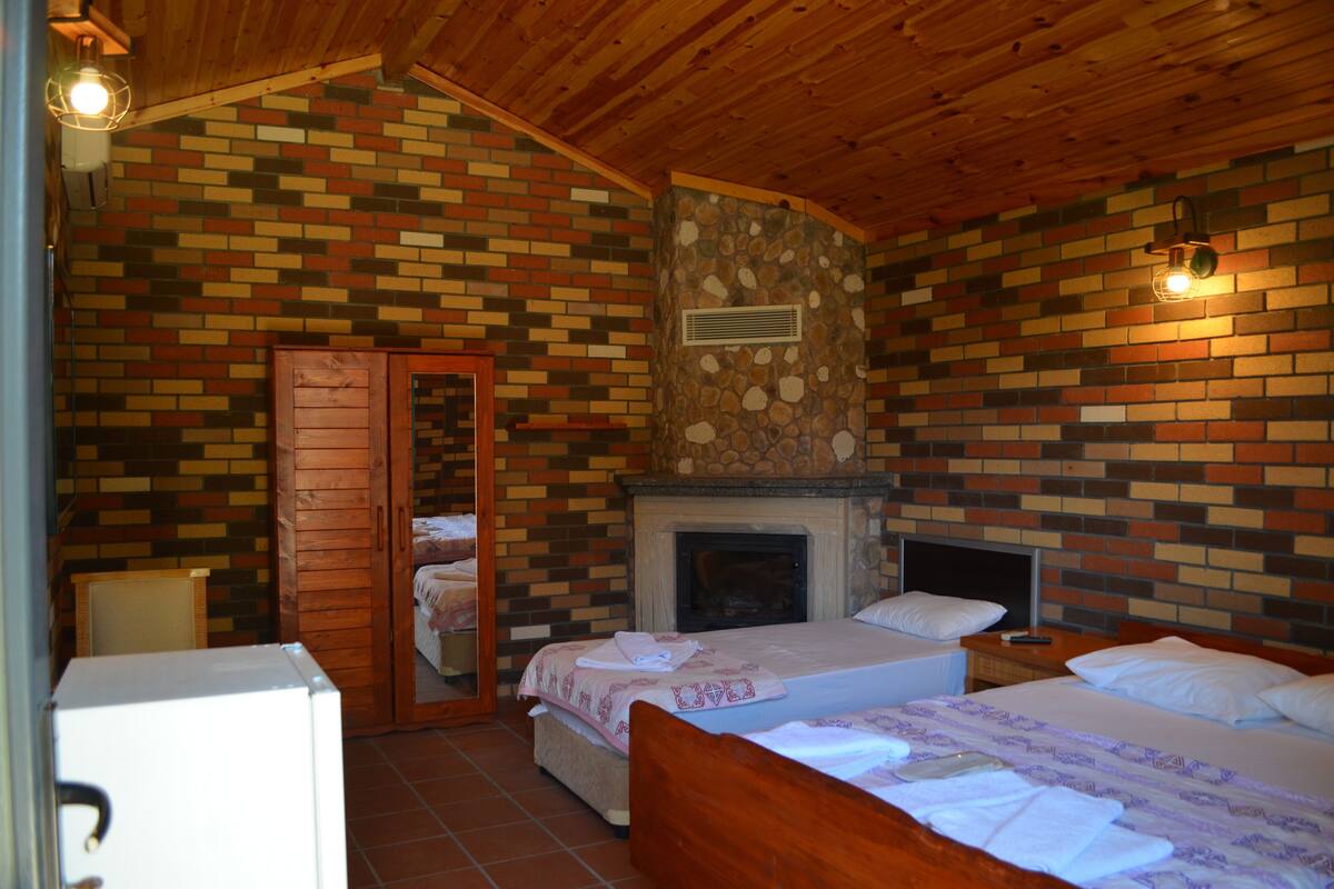 Un dormitorio con dos camas, una pared de ladrillo, una chimenea de piedra y vigas de madera en el techo.