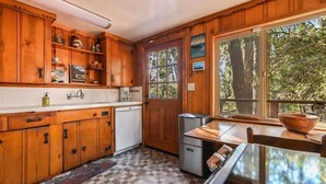Une cuisine en bois avec un carrelage à motifs, un réfrigérateur, une machine à café et une fenêtre donnant sur les arbres.