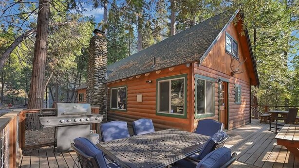 Une cabane en rondins dotée d’une terrasse, d’un barbecue extérieur et d’un espace salon.