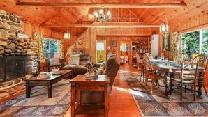 L’intérieur d’un chalet confortable, avec une cheminée en pierre, des murs en bois, un coin repas et un lustre.