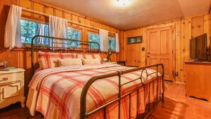 Une chambre dans une cabane en bois, avec un lit en métal, une table de chevet et un téléviseur.