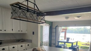 Una cocina con una isla de madera, armarios blancos y vistas a un lago a través de la puerta abierta.