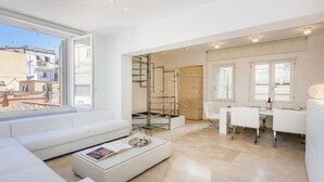 Una sala de estar moderna con un sofá blanco, una mesa de centro de vidrio y un comedor con una mesa y sillas blancas.