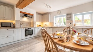 A modern kitchen with white cabinets, a wooden ceiling, and a breakfast setup on the dining table.
