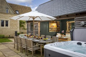 Una terraza de madera con una mesa de comedor, sillas y un jacuzzi.