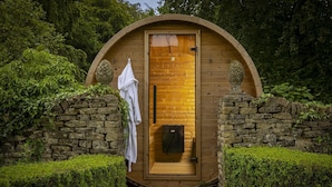 Une structure circulaire en bois, dotée d’une porte, d’une serviette accrochée au mur et d’un mur en pierre sur un des côtés.
