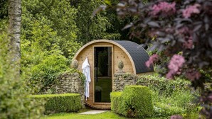 Une petite structure en bois, dotée d’une arche et d’un mur en pierre, avec une porte et une serviette accrochée à cette porte.