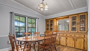 Ein Esszimmer mit Holztisch und -stühlen, großen Fenstern und einem Holzschrank mit Glastüren.