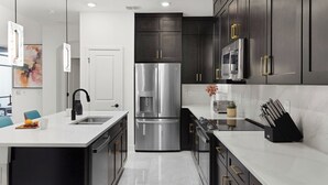 A modern kitchen with dark cabinets, stainless steel appliances, and a marble countertop.