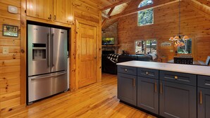 Interior de una cabaña con paredes de madera, una chimenea de piedra, una cocina amplia con electrodomésticos de acero inoxidable y un rincón de estar acogedor.