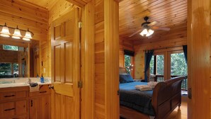Un dormitorio de cabaña de madera con una cama, un ventilador de techo y un ventanal grande.