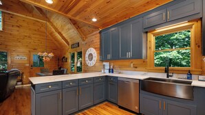 Cocina estilo cabaña con paredes de madera, un reloj grande y una ventana con vista a árboles.
