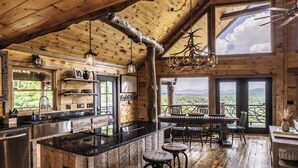 A rustic cabin with a large wooden interior, a central island bar, and a dining area with a view of the mountains. - Lookout Lodge- Blue Ridge GA (Blue Ridge)