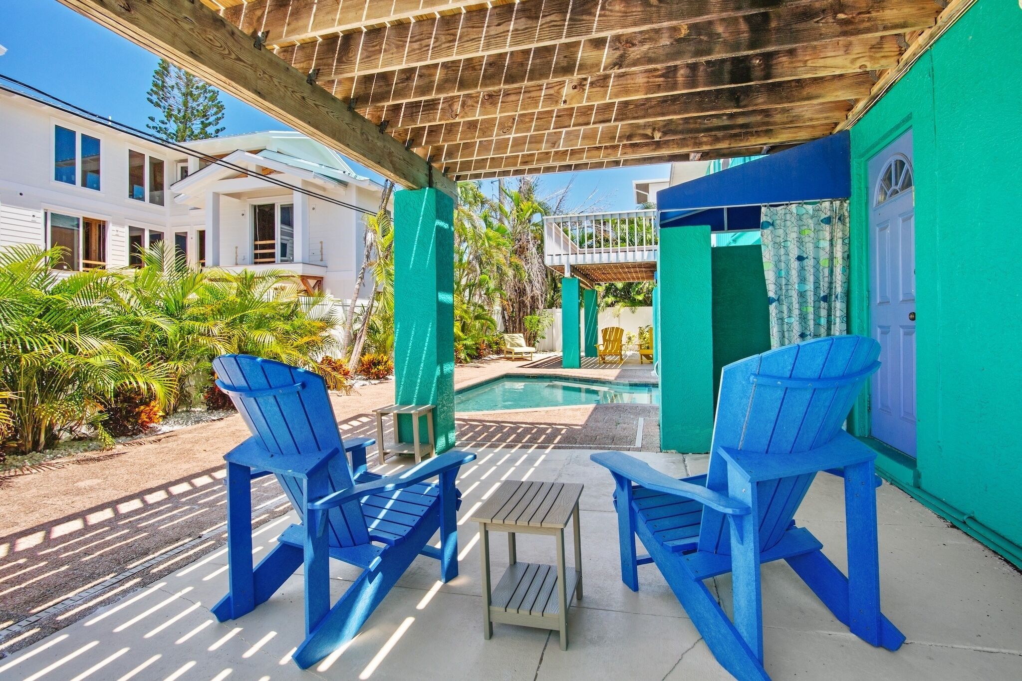 A covered outdoor area with blue Adirondack chairs, a small table, and a pool.