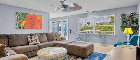 A living room with a sectional sofa, a round coffee table, a ceiling fan, and a view of the outdoors through large windows.