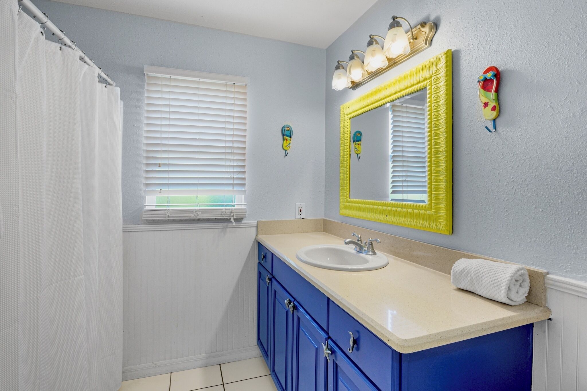 A bathroom with a white sink, blue cabinets, a yellow-framed mirror, and a shower curtain.