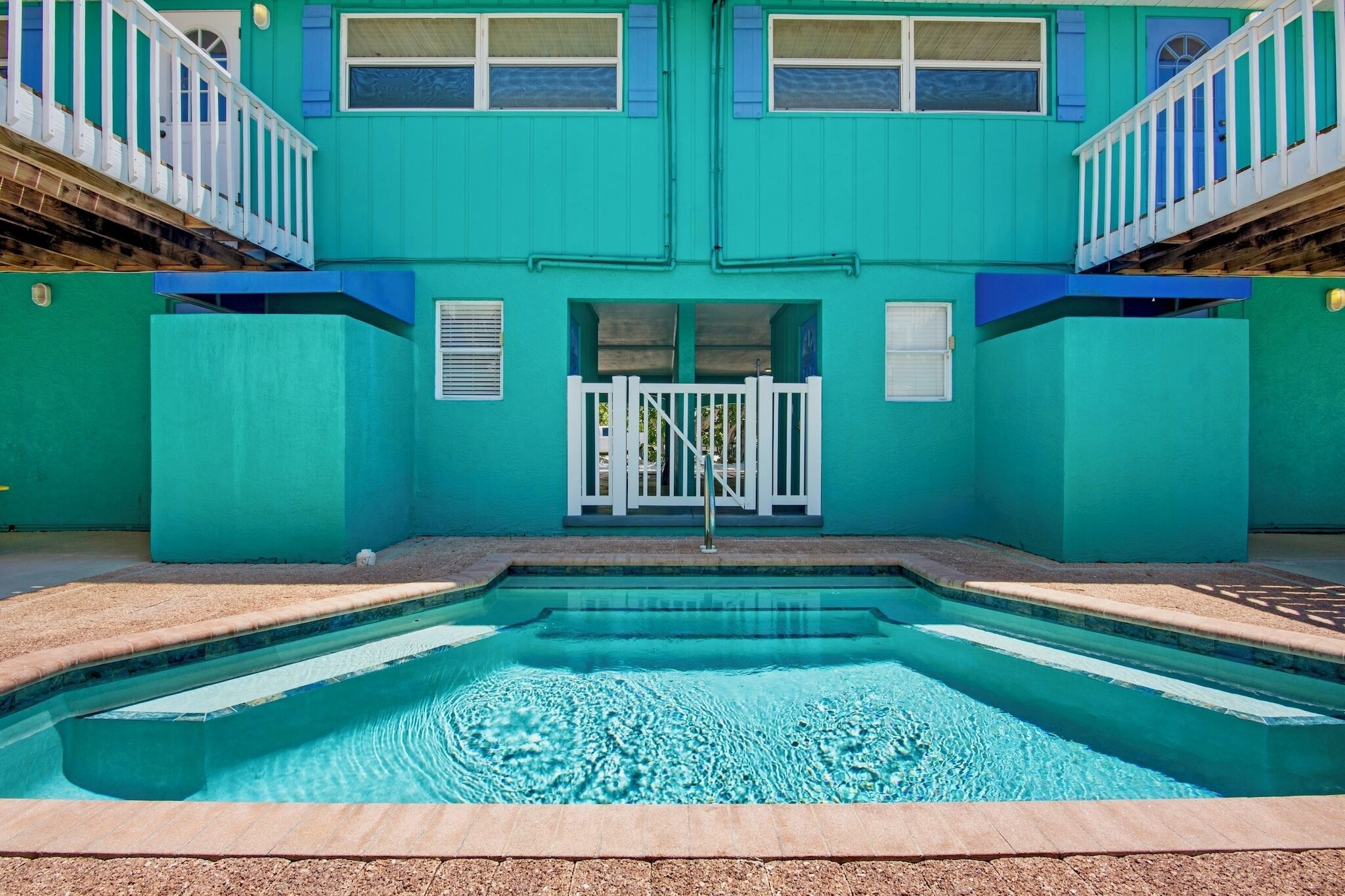 Ein türkisfarbenes Gebäude mit Schwimmbecken, weißen Geländern und einem verschlossenen Eingang.
