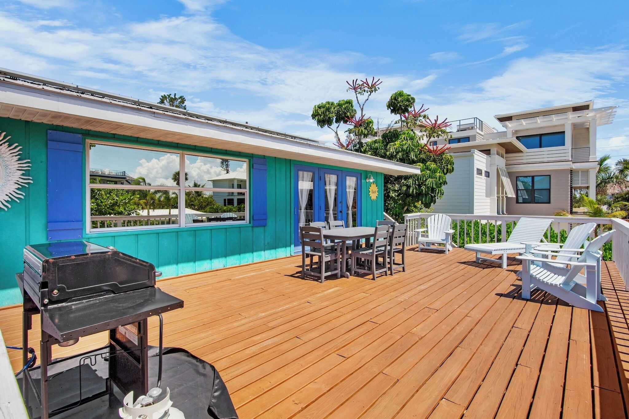 A wooden deck with a barbecue grill, outdoor seating, and a modern house with blue and white exterior walls.