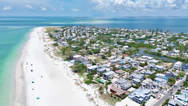An aerial view of a coastal residential area with a sandy beach, houses, and a river. - Emerald Shores East! Walk to Beach! (Anna Maria)