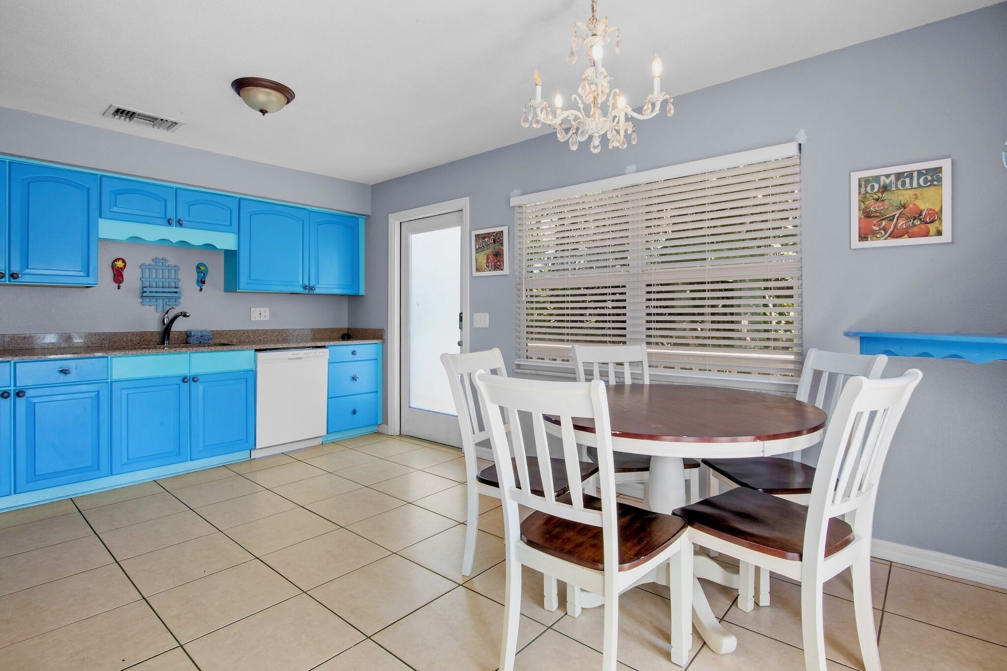 A kitchen with blue cabinets, a white dishwasher, and a dining area with a round table and white chairs.