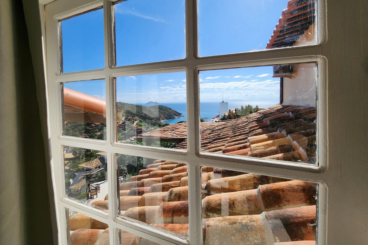 A window with a view of terracotta roof tiles and a coastal landscape.