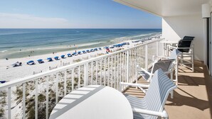 Un balcon donnant sur une plage, avec des chaises blanches et une table.