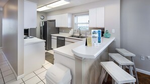 Une cuisine moderne avec des meubles blancs, un réfrigérateur en acier inoxydable, un four encastré et un petit îlot central doté de tabourets.