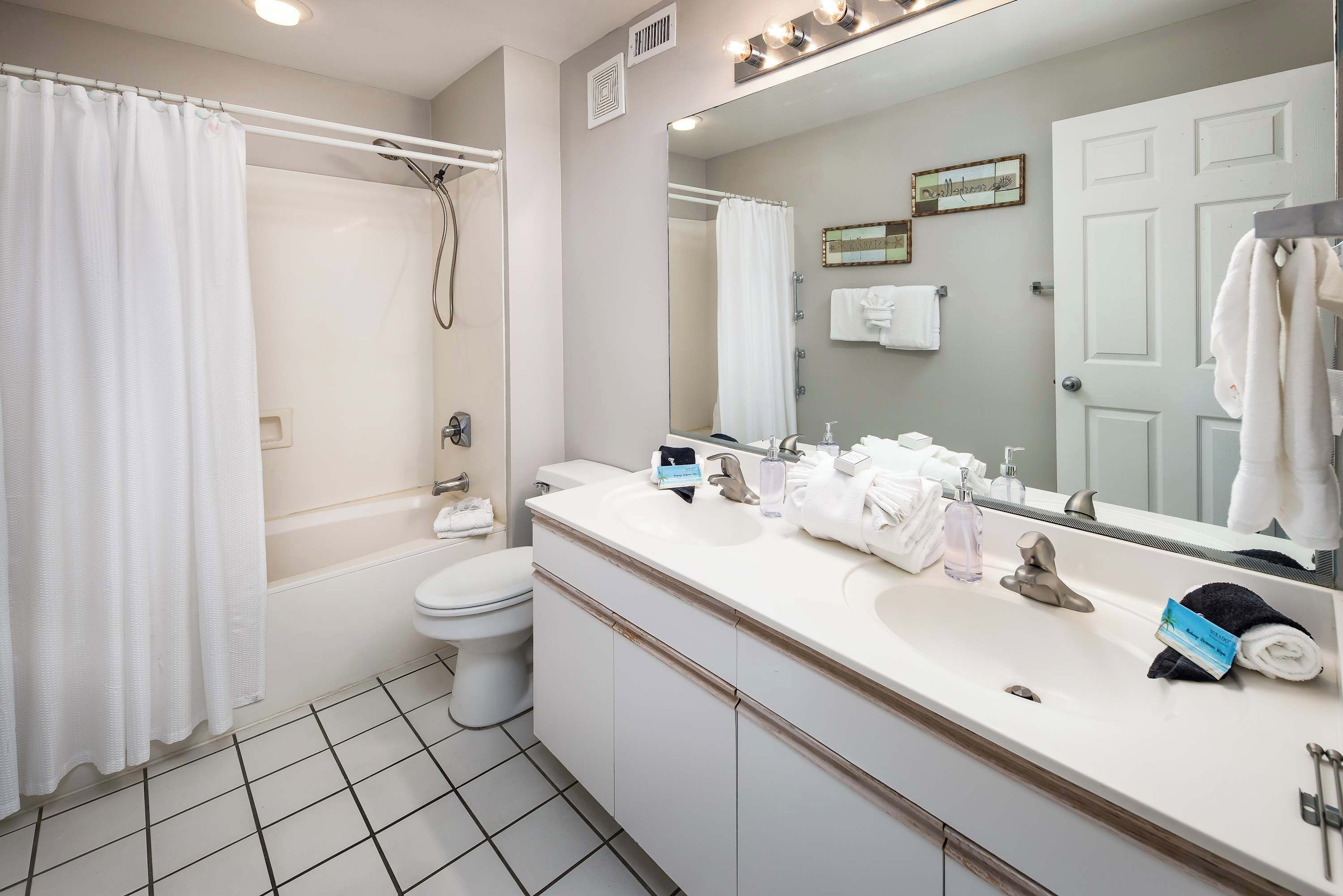 A modern bathroom with a bathtub, toilet, and a large vanity with a mirror.