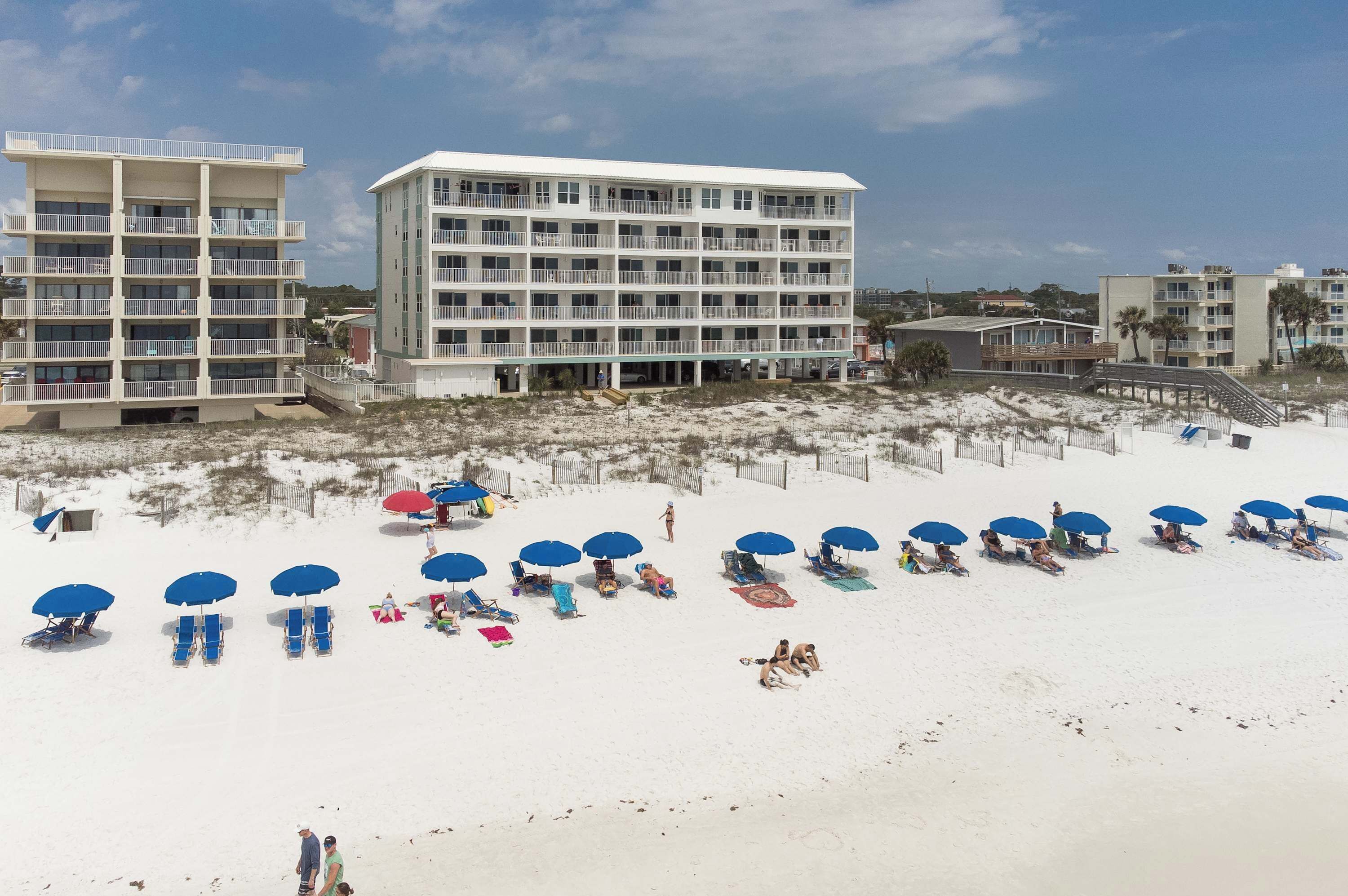 Ein Strandhotel mit mehreren Balkonen, ein Sandstrand mit Sonnenschirmen und einem klaren Himmel.